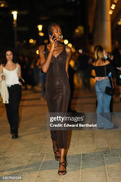 Guest wears a gold chain pendant necklace, a brown V-neck / tank-top / long tube dress, a black shiny leather shoulder bag, black shiny leather...