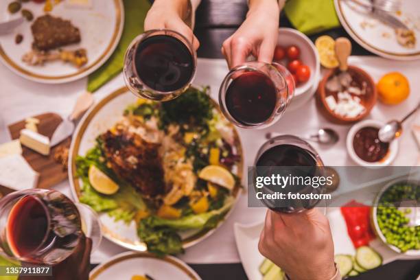 nahaufnahme von freunden, die während des thanksgiving-essens mit gläsern rotwein jubeln - friends toasting above table stock-fotos und bilder