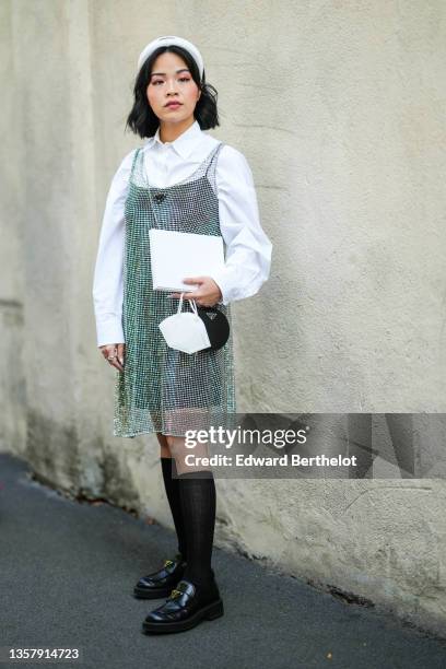 Guest wears a white headband from Prada, a white shirt, a rhinestones tank-top dress from Prada, a black shiny leather crossbody bag from Prada, a...