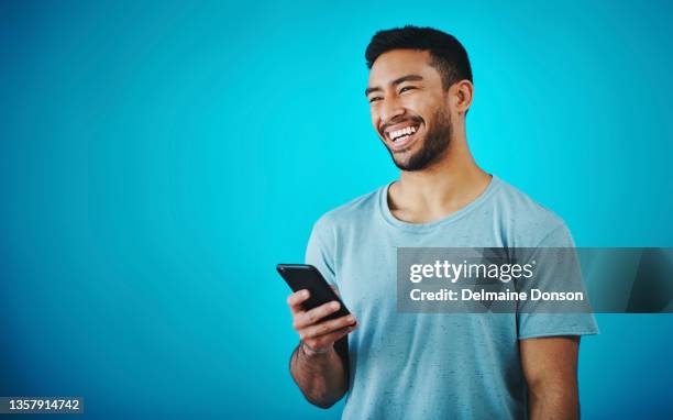 shot of a handsome young man holding a cellphone while standing against a blue background - man studio shot stock pictures, royalty-free photos & images