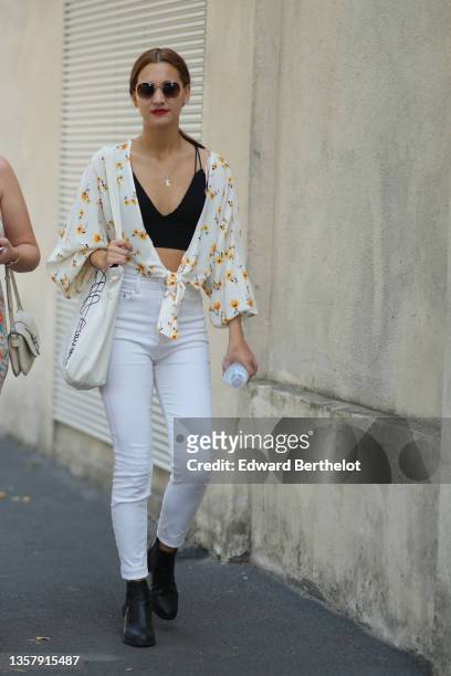 Guest wears sunglasses, earrings, a silver chain pendant necklace, a black ribbed V-neck cropped top, a white with yellow and black flower print...