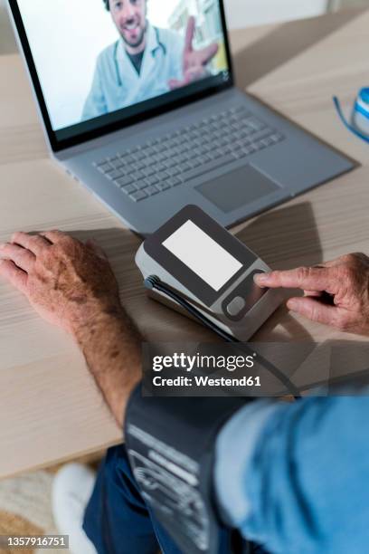 man measuring blood pressure during video call with doctor at home - medical technology stock-fotos und bilder