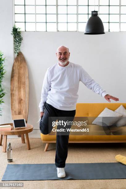 active senior man stretching legs on exercise mat at home - on one leg stock pictures, royalty-free photos & images