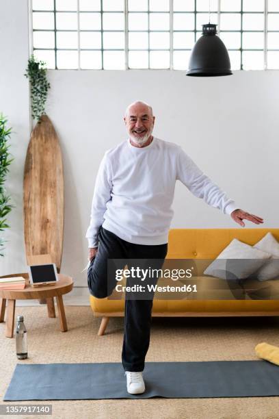 active senior man stretching legs on exercise mat at home - stå på ett ben bildbanksfoton och bilder