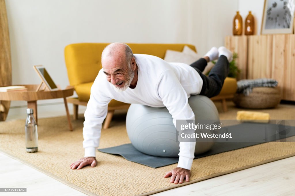 Active senior man exercising on fitness ball at home