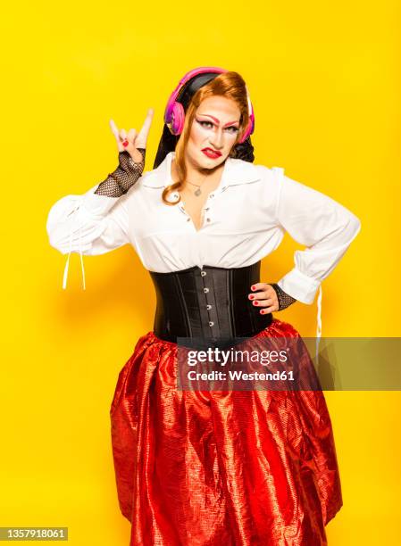 drag queen listening rock music and gesturing horn sign against yellow background - travesti imagens e fotografias de stock