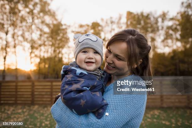 mother carrying cheerful baby boy at lawn - eastern european descent stock pictures, royalty-free photos & images
