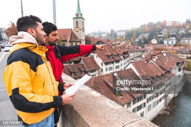 man pointing by friend holding map at bern canton, switzerland - bern clock tower stock pictures, royalty-free photos & images