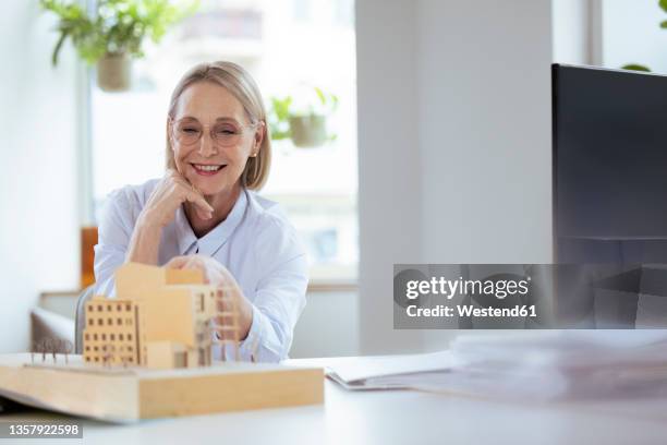 smiling businesswoman checking model at workplace - architekturmodell stock-fotos und bilder