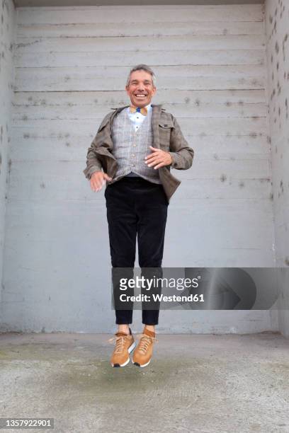 happy man jumping in front of gray wall - one man only imagens e fotografias de stock