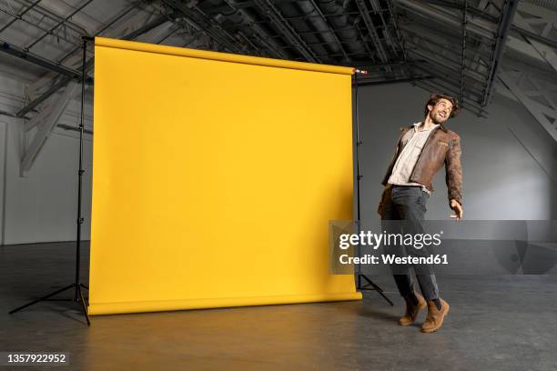 smiling businessman on tiptoe by yellow backdrop - tiptoe stock-fotos und bilder