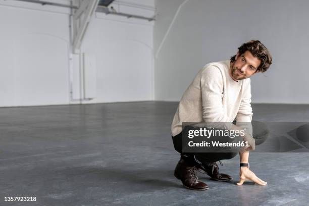 smiling businessman crouching in industrial hall - hombre agachado fotografías e imágenes de stock