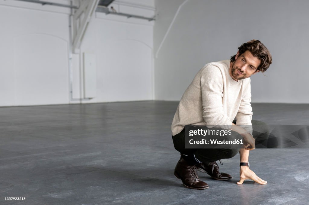 Smiling businessman crouching in industrial hall