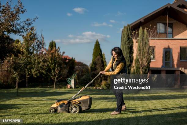 woman mowing grass with lawn mower on sunny day - cortacésped manual fotografías e imágenes de stock