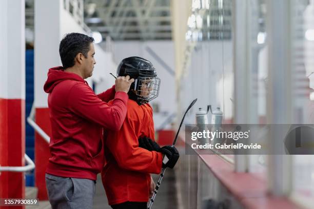 padre ayudando a su hijo a prepararse para el entrenamiento - hockey fotografías e imágenes de stock