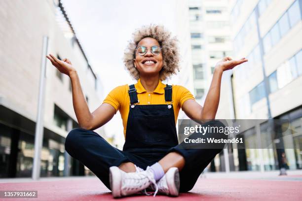 smiling woman meditating on footpath - schneidersitz stock-fotos und bilder