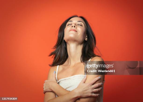 smiling woman with eyes closed hugging self against orange background - cabeça para trás - fotografias e filmes do acervo