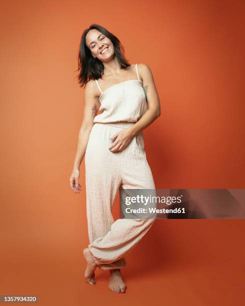 smiling woman standing with legs crossed at ankle against background - kopf zur seite neigen stock-fotos und bilder