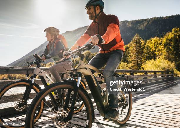 smiling mature couple riding bicycles on bridge - fahrrad paar stock-fotos und bilder