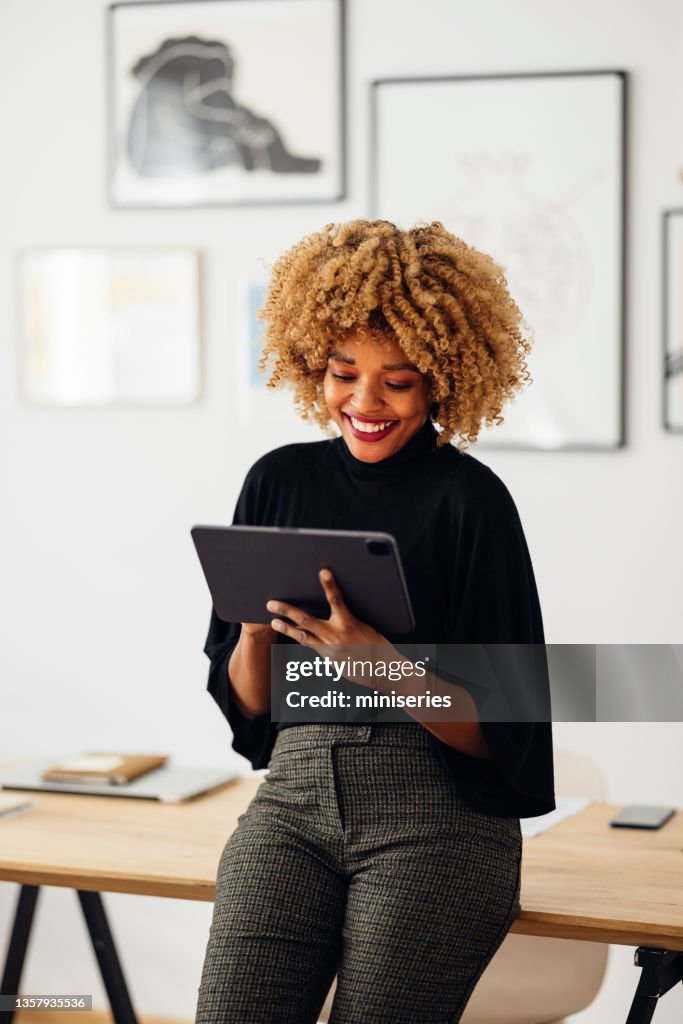 Glückliche Geschäftsfrau, die mit ihrem Tablet auf ihrem Schreibtisch sitzt