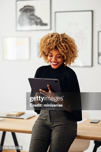 Feliz mujer de negocios sentada en su escritorio usando su tableta Feliz mujer de negocios sentada en su escritorio usando su tableta