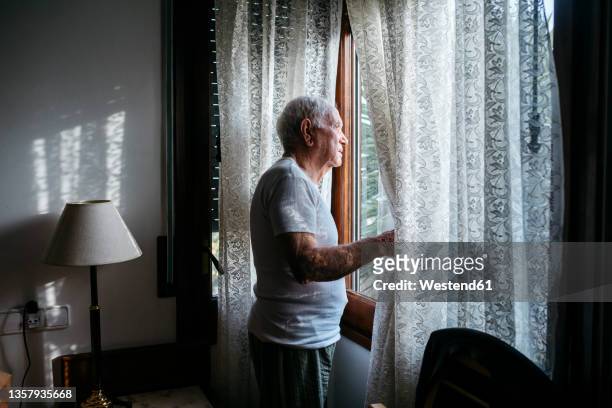 man looking through window at home - solitudine foto e immagini stock