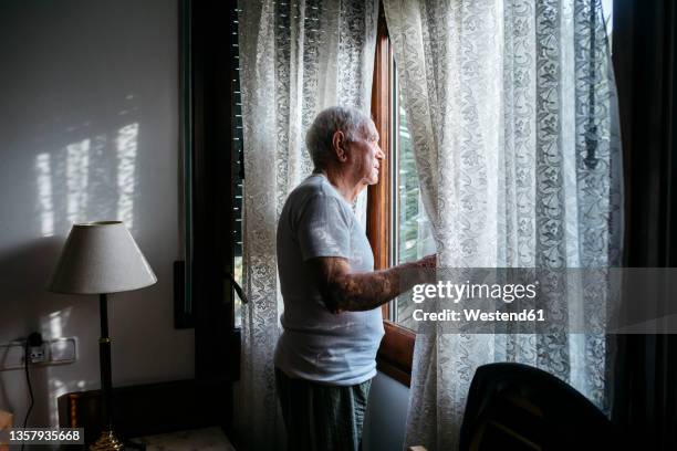 man looking through window at home - idosos imagens e fotografias de stock