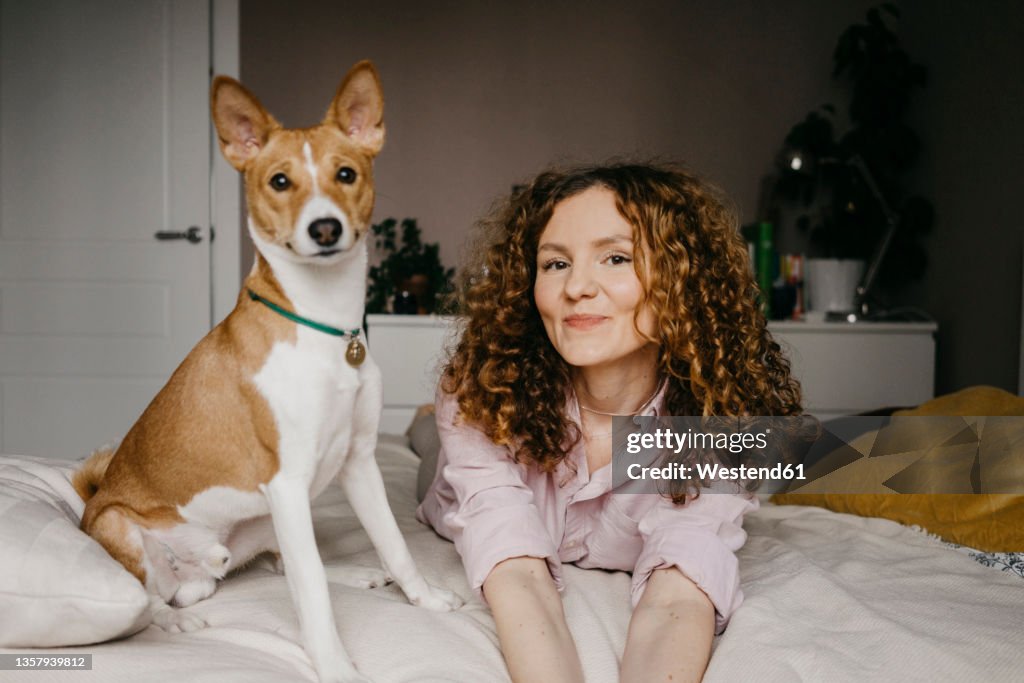 Smiling woman lying on bed with dog in bedroom
