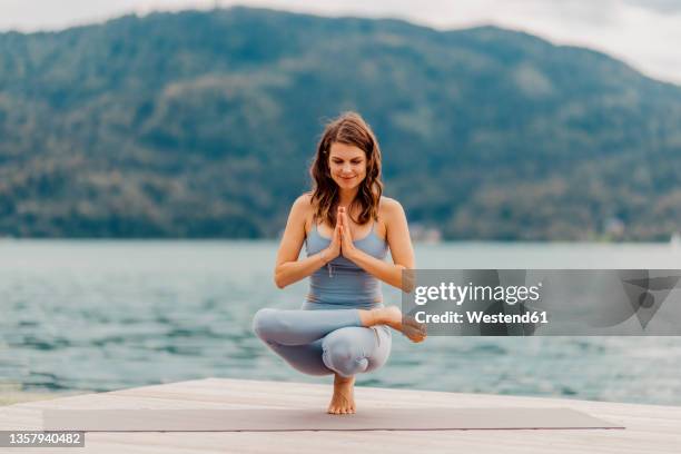 smiling woman practicing toe stand on jetty in front of lake - kärnten am wörthersee stock pictures, royalty-free photos & images
