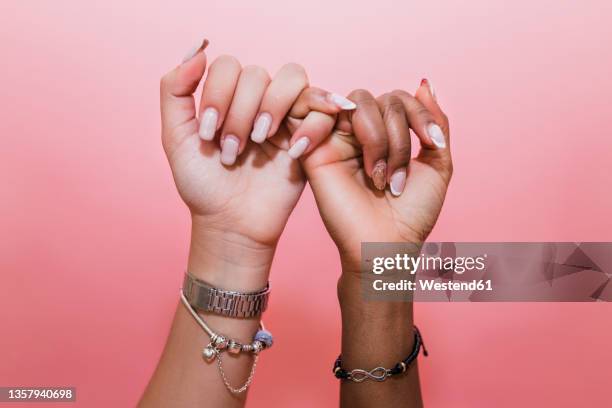 lesbian couple making pinky promise against pink background - promise stock-fotos und bilder