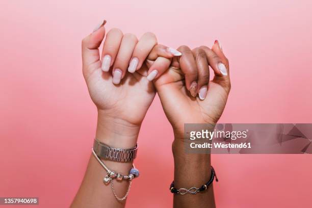 lesbian couple making pinky promise against pink background - oath 個照片及圖片檔