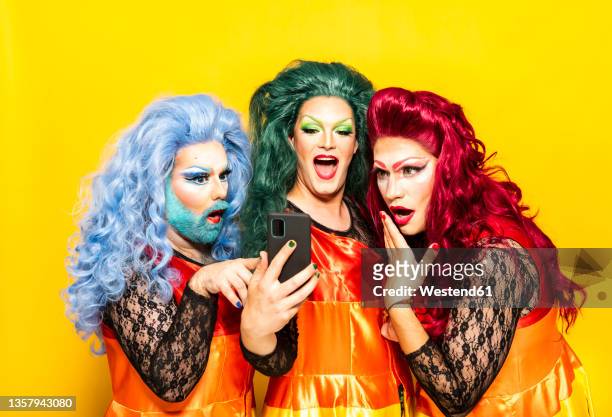 surprised drag queens using mobile phone against yellow background - drag queen stockfoto's en -beelden