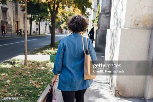 a back view of an anonymous female going home after work with lots of paper bags - green shirt stock pictures, royalty-free photos & images