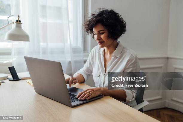 una hermosa mujer afroamericana trabajando en línea en su computadora portátil - laptop fotografías e imágenes de stock