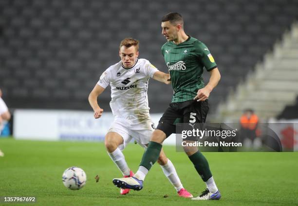 James Wilson of Plymouth Argyle plays the ball as Scott Twine of Milton Keynes Dons looks on during the Sky Bet League One match between Milton...