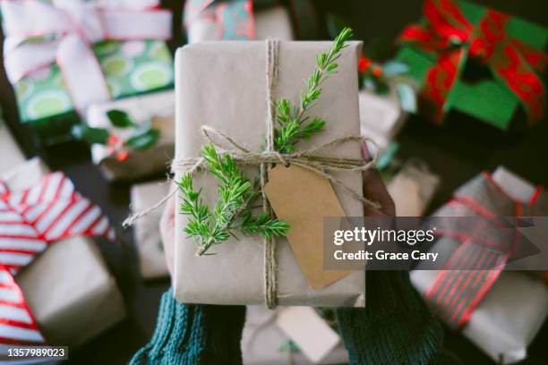woman holds christmas present adorned with juniper branch - black craft paper stock pictures, royalty-free photos & images