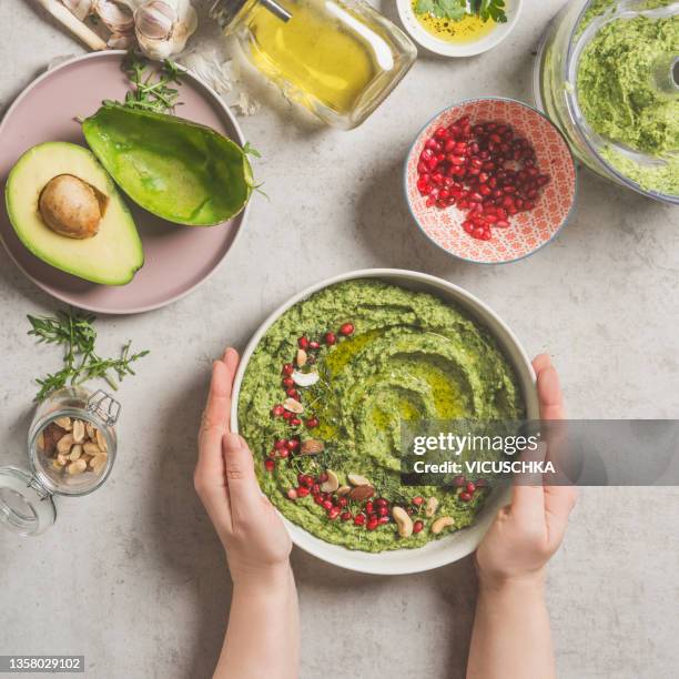 woman hands holding bowl with avocado dip on pale grey concrete table with ingredients - avacado oil stock pictures, royalty-free photos & images