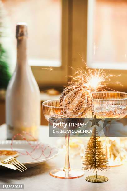 silvester table setting with champagne glasses with christmas bauble with burning sparkler, christmas tree, champagne bittle and cutlery at window background - food and drink imagens e fotografias de stock