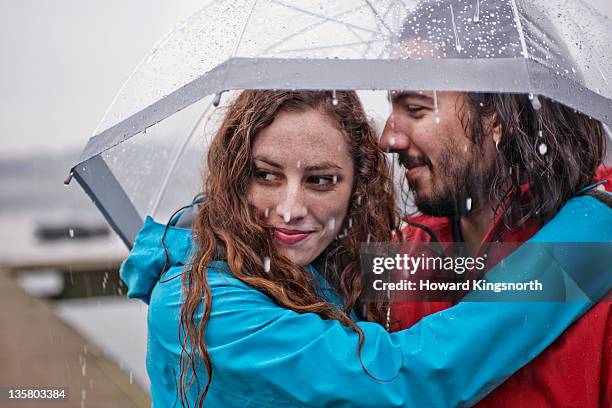 couple embracing underneath umbrella - rain couple stockfoto's en -beelden