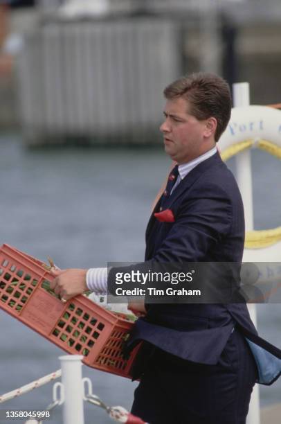 Royal valet Michael Fawcett carrying a plastic crate of vegetables on the quayside at Heysham Port, Lancashire, England, 7th August 1989. The Royal...