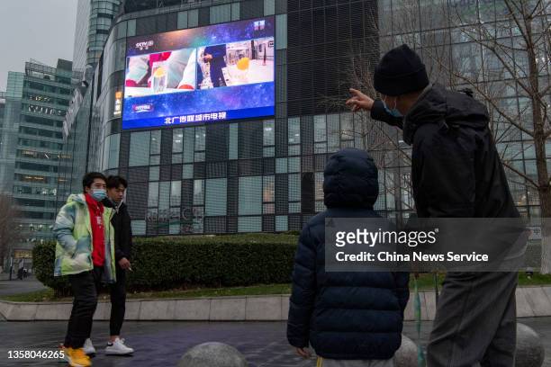 Man and his child watch an outdoor screen displaying the first 'Tiangong Class', live lecture delivered by Chinese astronauts Zhai Zhigang, Wang...