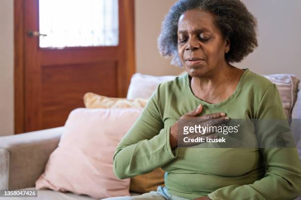 elderly woman having chest pain in living room - heart attack stock pictures, royalty-free photos & images