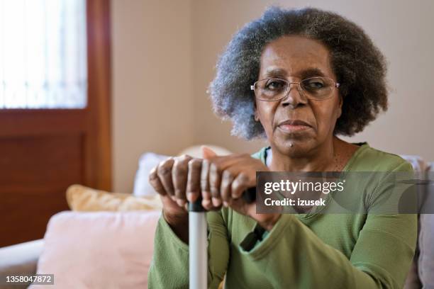 ältere frau mit gehstock zu hause - african american woman serious stock-fotos und bilder