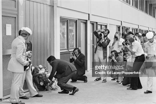 Press photographers take pictures as a man lays flowers next to a wreath placed beside the door to the Israel team's accomodation in the Olympic...