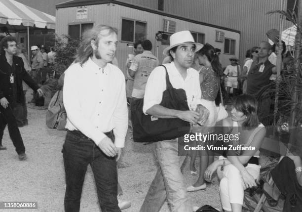 American singer, songwriter and musician Tom Petty , wearing a white shirt and walking with a man wearing a Panama hat backstage at the Live Aid...