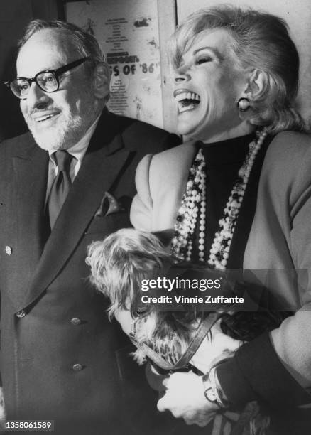 German-born British film and tv producer Edgar Rosenberg with his wife, American comedian Joan Rivers , wearing beaded necklaces, holding her...