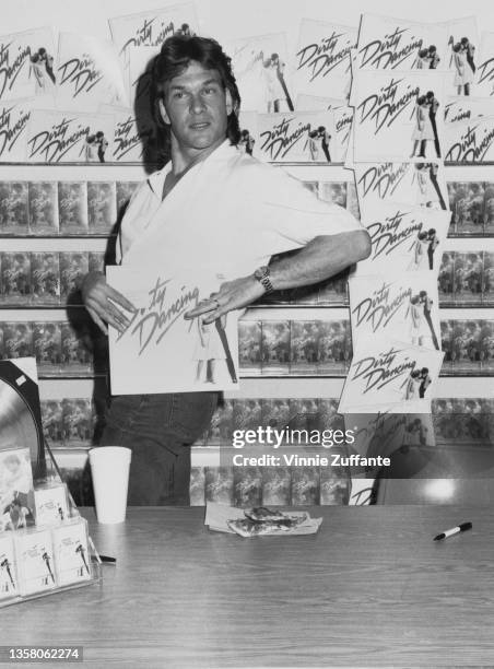 American actor, singer and dancer Patrick Swayze poses with an LP cover as he attends an in-store promotional event, signing copies of the soundtrack...