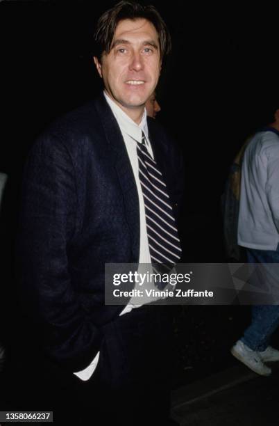 British singer and songwriter Bryan Ferry wearing a black suit over a white shirt with a black-and-white diagonally striped tie, his hands in his...