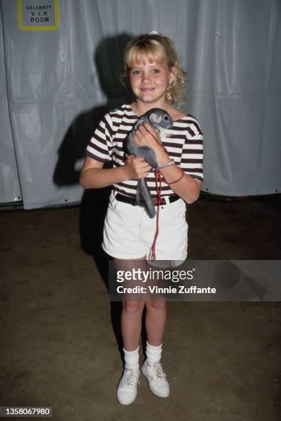 America child actress Candace Hutson, wearing a black-and-white hooped t-shirt and white shorts, holding her pet chinchilla Charlie, circa 1990.