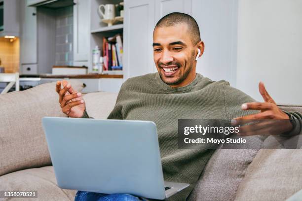 shot of a young man using his laptop to make a video call while working from home - in ear headphones stock pictures, royalty-free photos & images